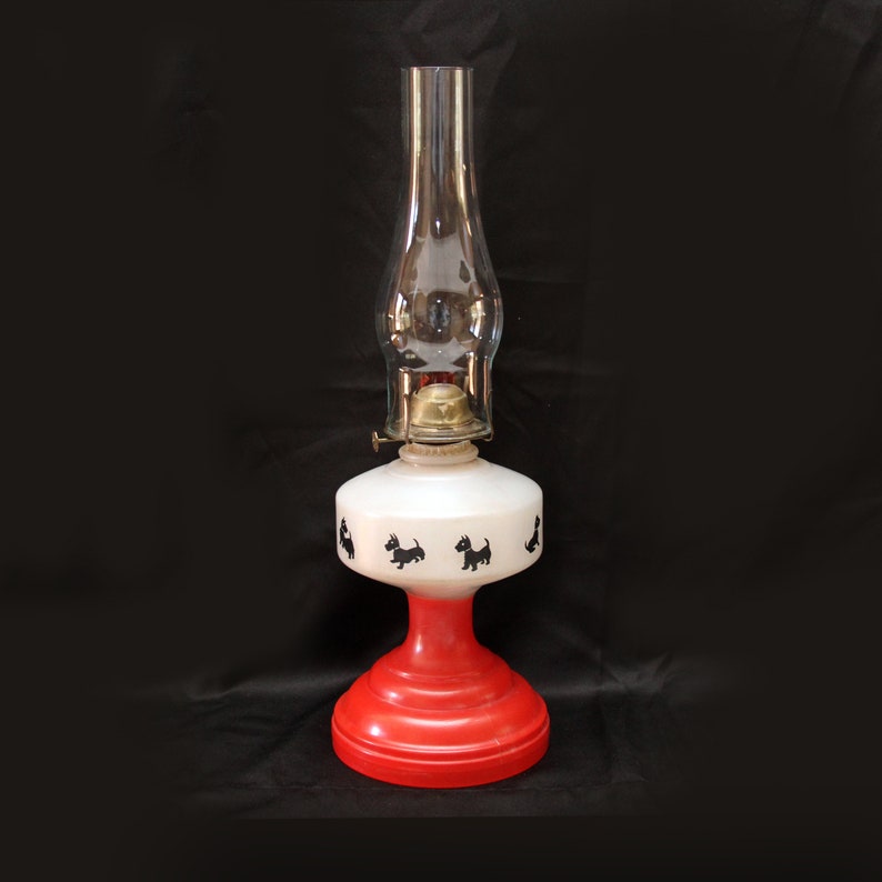 May include: A red and white oil lamp with a glass chimney and a design of black silhouettes of dogs.