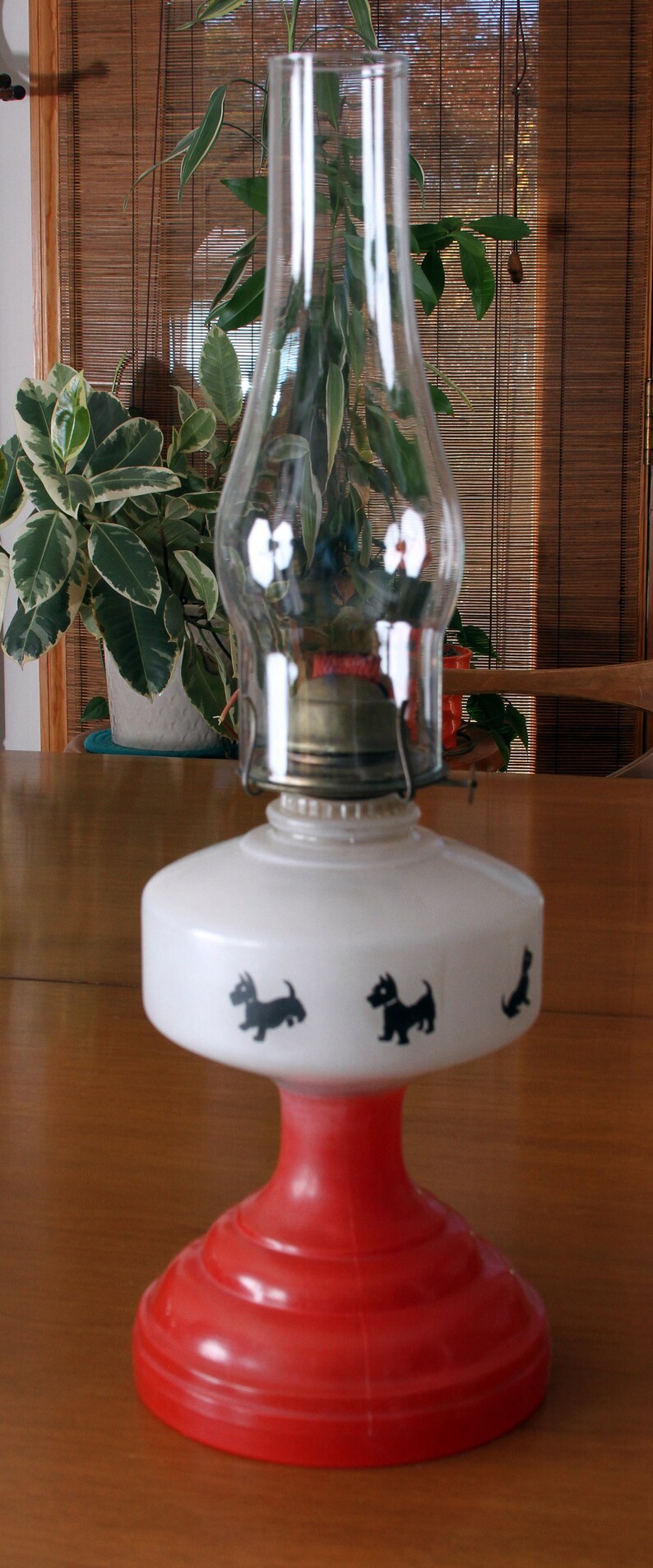 May include: A red and white oil lamp with a clear glass chimney. The lamp has a white base with black silhouettes of Scottish terriers.