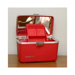 May include: A bright red rectangular vanity case with a silver-toned metal trim and a secure latch closure. The lid opens to reveal an interior mirror and a removable red plastic tray with three compartments. The front features a silver Starlite logo.