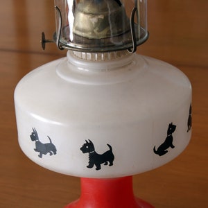 May include: A white oil lamp with a red base and black silhouette images of Scottish Terriers around the body.