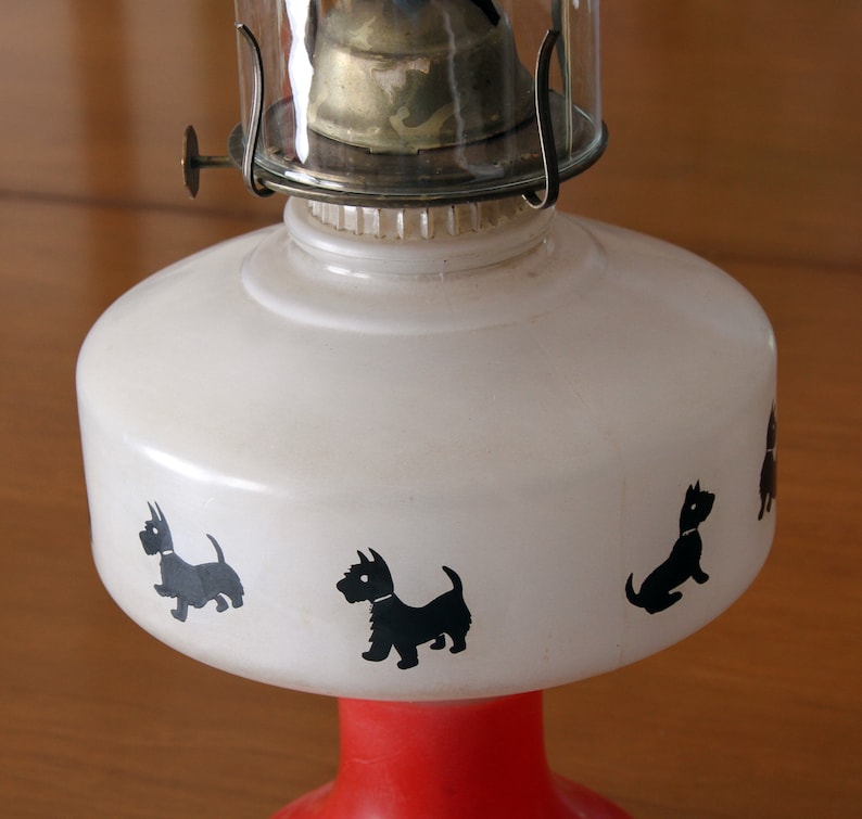 May include: A white oil lamp with a red base and black silhouette images of Scottish Terriers around the body.