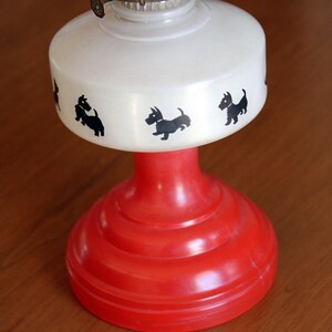 May include: A white oil lamp with a red base and black silhouette images of Scottish Terriers around the top.