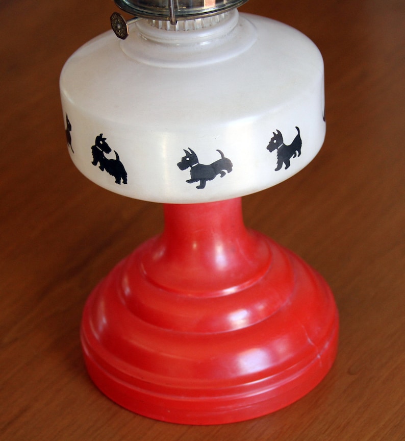 May include: A white oil lamp with a red base and black silhouette images of Scottish Terriers around the top.