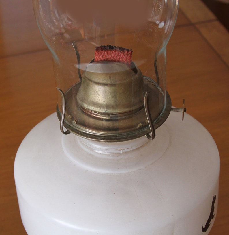 May include: A white glass oil lamp with a brass burner and a red wick. The lamp has a clear glass chimney.