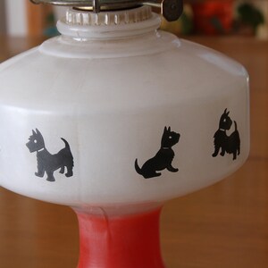 May include: White oil lamp with a red base and black silhouette images of Scottish Terriers around the lamp.