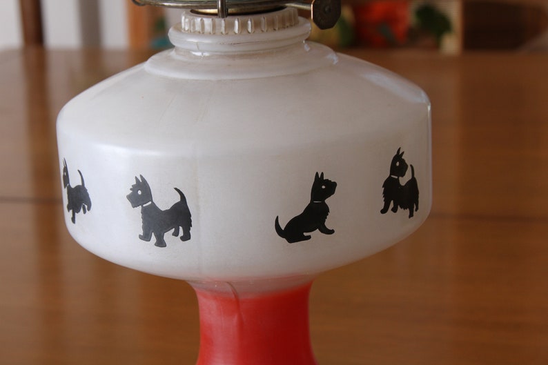 May include: White oil lamp with a red base and black silhouette images of Scottish Terriers around the lamp.