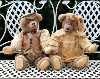 May include: Two teddy bears dressed in vintage clothing sit on a white metal bench. The bear on the left is wearing a brown and white striped vest, a brown and white striped hat, and a brown and white striped bow tie. The bear on the right is wearing a brown dress with a white collar and a white bow. Both bears have brown fur and are sitting upright.