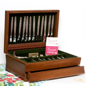 May include: A wooden flatware chest with a dark green velvet interior containing silver-plated knives and forks. The set includes a Community brand plaque and a pink guarantee card with the text Garantie L'Argenterie Community printed on it.