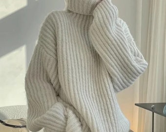 以下が含まれることがあります： リブ編みの白い厚手のタートルネックセーター。長袖でゆったりとしたフィット感です。