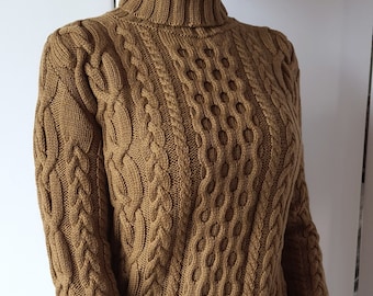 May include: A brown cable knit turtleneck sweater with a loose fit.