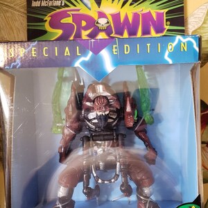 May include: A Mutant Spawn Ultra-Action Figure in a Special Edition box. The figure is a detailed, articulated action figure with a dark color scheme. The box features the Spawn logo and the text "Transforming Action!"