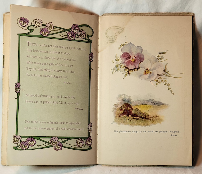 May include: Open book with text and illustrations. The left page has a poem with floral border. The right page features a floral illustration of purple and white pansies, and a landscape scene. The text reads, "The pleasantest things in the world are pleasant thoughts."