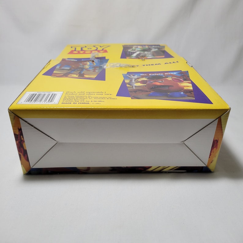 Peut inclure: Bo&icirc;te en carton jaune sur le th&egrave;me de Toy Story. La bo&icirc;te pr&eacute;sente des images de Woody, Buzz l'&Eacute;clair et M. Patate. Le texte sur la bo&icirc;te indique "Toy Story" et "Collectionnez-les tous !". La bo&icirc;te est fabriqu&eacute;e en Chine.