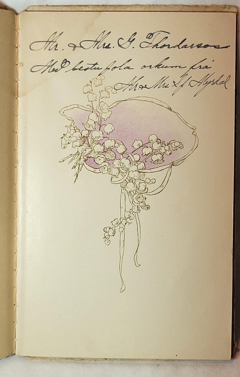 May include: An open book page with handwritten text and a floral illustration. The illustration features a hat shape in light purple with white flowers and ribbons. The text is in cursive.