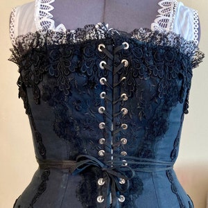 May include: Black corset with black lace trim and silver eyelets. The corset is laced up the back with black ribbon.