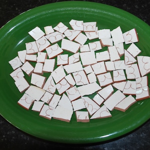May include: A green plate filled with white ceramic tiles, each with a unique design. The tiles are broken into various shapes and sizes.