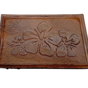 May include: A rectangular, brown, textured doormat featuring a raised floral design of three hibiscus flowers. The mat has a framed border and is made of a durable material suitable for outdoor use.