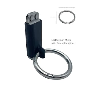 Puede incluir: Una multiherramienta Leatherman Micra negra con un mosquetón redondo plateado. La herramienta está unida al mosquetón con una funda de plástico negra. "All Key Chains Come with one 1" key Ring as well" está escrito en la esquina superior derecha de la imagen.