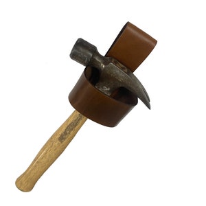 May include: A brown leather hammer holder with a hammer attached. The hammer has a wooden handle and a metal head.