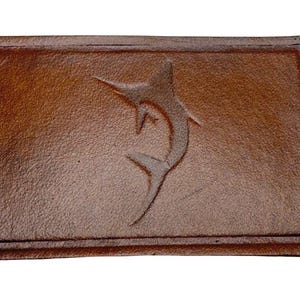 Può includere: Un cerotto in pelle marrone con un design in rilievo di un pesce marlin.