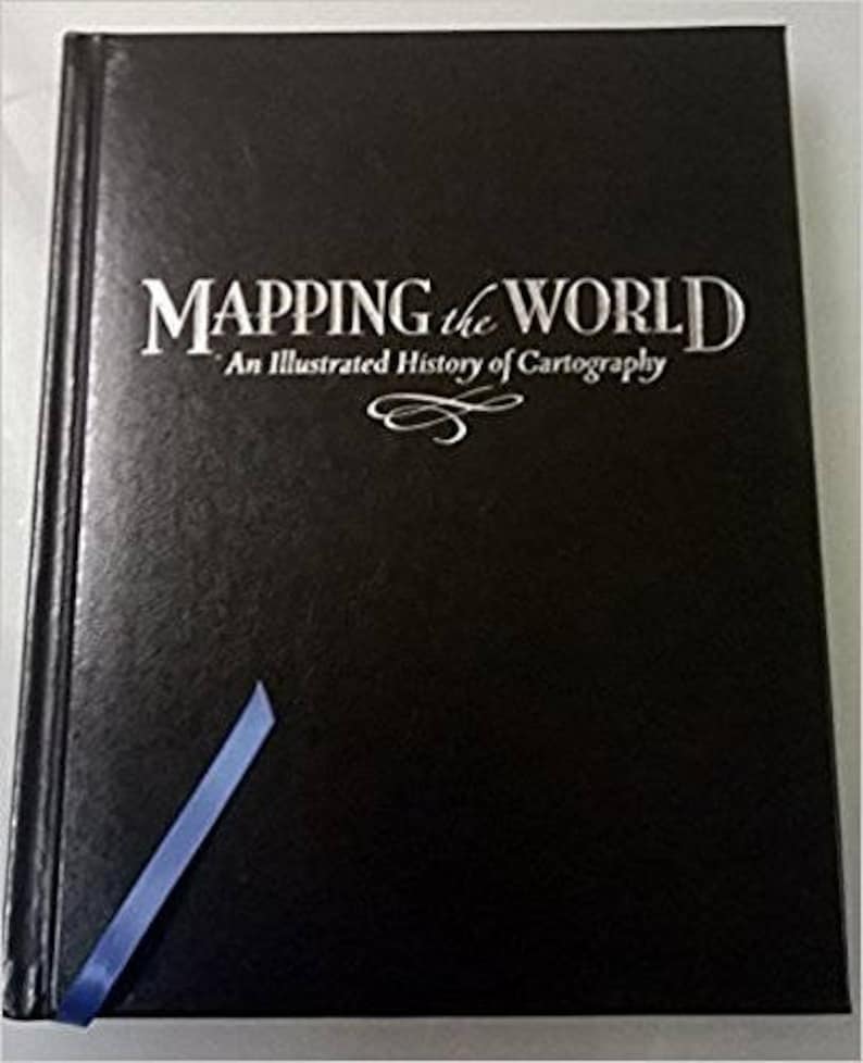 May include: A hardcover book titled "MAPPING the WORLD" with the subtitle "An Illustrated History of Cartography" in silver lettering on a black cover. A blue ribbon bookmark is visible. The book's cover is dark and textured.