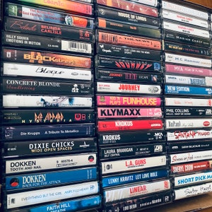 May include: A collection of vintage cassette tapes featuring various artists and albums, including Mariah Carey, Journey, Huey Lewis and the News, and more. The tapes are arranged vertically in a stack, with the titles and artist names visible on the front of each tape.