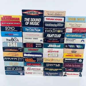 May include: A stack of VHS tapes featuring a variety of movie titles, including "The Scorpion King", "The Sound of Music", "Thelma & Louise", "The Wiz", "Fight Club", "The Insider", "Jackal", "Just Married", "Animal House", "Lean on Me", "My Stepmother is an Alien", and "Rush Hour".