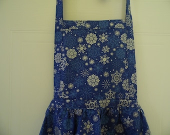 May include: A blue apron with a snowflake pattern. The apron features a dark blue background with white and light blue snowflakes. It has a ruffled bottom and a neck strap.