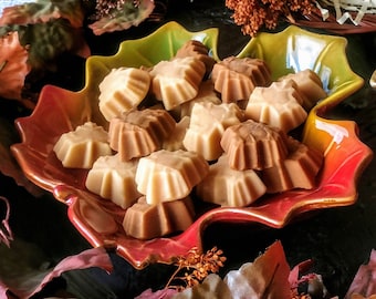 May include: A red and green leaf-shaped ceramic dish filled with maple leaf-shaped candies. The candies are a mix of light and dark brown colors.