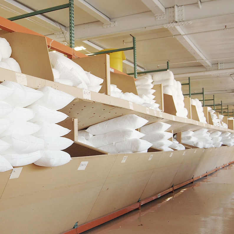 May include: A warehouse storage system with multiple shelves filled with white pillows. The shelves are made of wood and have a slanted design to allow for easy access to the pillows.