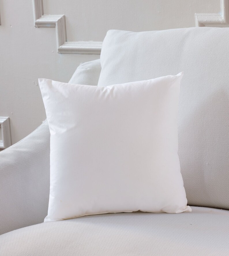 May include: A white pillow on a white couch. The pillow is square and has a smooth surface.