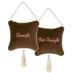May include: Two brown velvet decorative pillows with the words "Tonight" and "Not Tonight" embroidered in pink script. Each pillow has a cream-colored border, a cream tassel, and a cream rope for hanging.