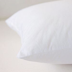May include: A white pillow with a smooth, soft fabric surface. The pillow is folded in half and the seam is visible.