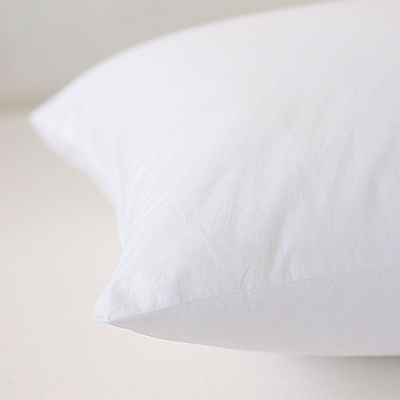 May include: A white pillow with a smooth, soft fabric surface. The pillow is folded in half and the seam is visible.
