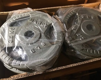 May include: Two sets of gray cast iron weight plates, each set wrapped in clear plastic. The plates are 2.5 kg each and have the word "MARCY" printed on them.
