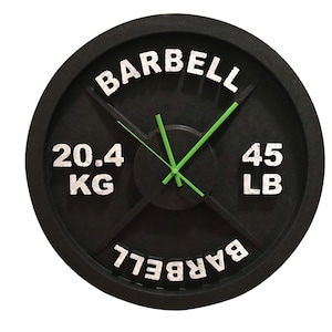 May include: Black weight plate clock with white text that reads "BARBELL" and "20.4 KG 45 LB BARBELL". The clock has green hands.
