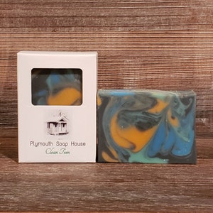May include: A bar of soap with a marbled design in shades of blue, yellow, and green, next to a white box with a window showing a similar soap. The box has the text "Plymouth Soap House Clean Teen".