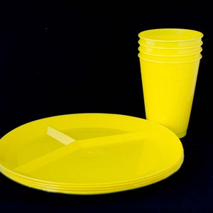 May include: A set of four bright yellow plastic cups stacked on top of each other, and a set of three bright yellow plastic divided plates stacked on top of each other.