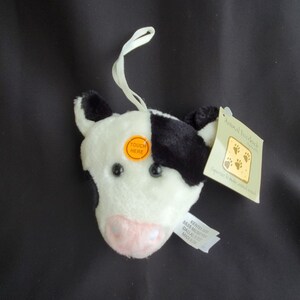 May include: A plush cow head with black and white fur, a pink nose, and black eyes. An orange sticker reads "TOUCH HERE." A tag reads "Animal Doorlock" with paw prints.