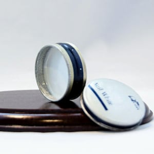 Puede incluir: Dos recipientes redondos blancos con ribete azul. Un recipiente tiene una franja azul y el texto "Nail White" en la parte superior. Los recipientes están sobre una superficie de madera marrón.