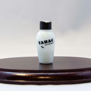 May include: A white bottle with a black cap and a black label that says "TABAC ORIGINAL" with a small black dog icon.