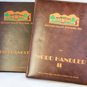 以下が含まれることがあります： 金色の文字で書かれた、茶色の革張り製マニュアルが2冊。左側のマニュアルのタイトルは「LIST HANDLER」、右側のマニュアルのタイトルは「THE WORD HANDLER II」。両方のマニュアルには、「SILICON VALLEY SYSTEMS, INC.」というロゴが記載されています。