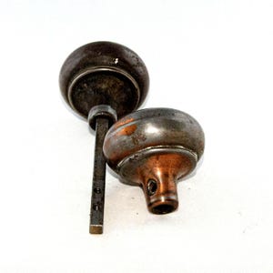 Op de afbeelding: Twee antieke deurknoppen, een met een koperen afwerking en de andere met een zilveren afwerking. Beide knoppen zijn rond en hebben een decoratief ontwerp.