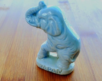 Può includere: Una statuetta di elefante in ceramica blu chiaro con la proboscide alzata. La statuetta è in piedi su una base che dice "GIAPPONE".