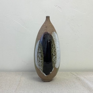 May include: A ceramic vase with a brown, green, black, and white abstract design. The vase is tall and narrow, with a rounded bottom and a slightly flared opening.