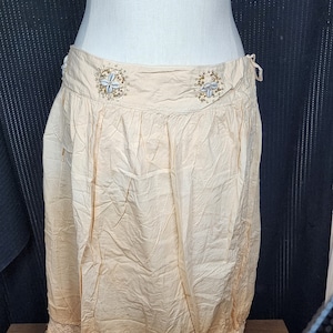 May include: A light beige skirt with a lace trim and beaded embellishments around the waist.