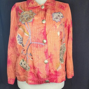 May include: A bright orange and pink jacket with a textured woven fabric and embroidered floral designs. The jacket has a collared neckline and a button closure.