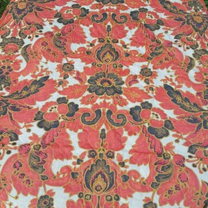 May include: A round tablecloth with a white background and a floral pattern in shades of red, black, and gold. The pattern features large, stylized flowers and leaves.