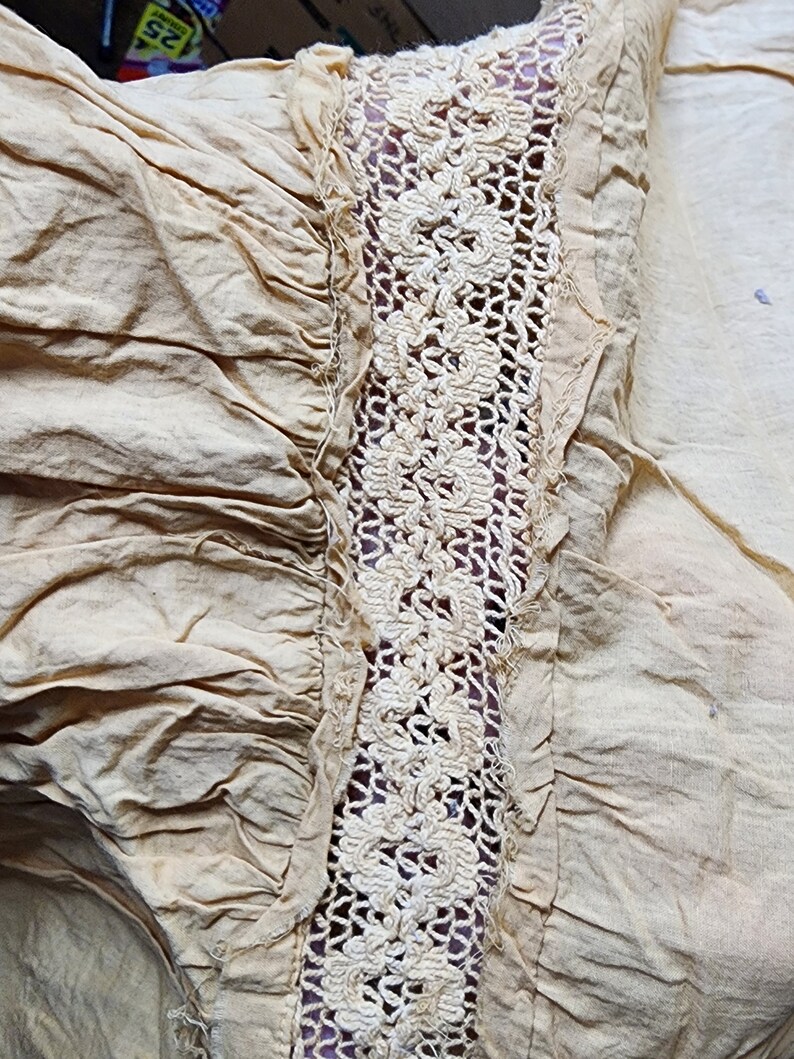 May include: Close-up of a beige fabric with a white crocheted trim. The fabric is gathered and has a slightly wrinkled texture.