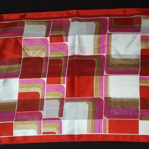 May include: A red, white, brown, and pink geometric patterned silk scarf. The scarf has a repeating pattern of squares and rectangles.